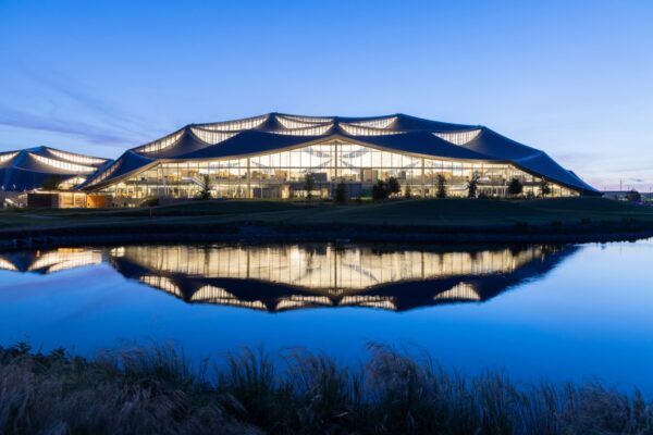 A photo of Bay View's larger building at twilight reflects in the stormwater retention pond, part of the water-positive design of the campus. Dragonscale | SunStyle